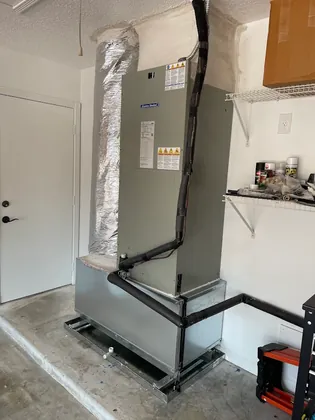 American Standard air handler on a raised stand in a garage with insulated refrigerant lines