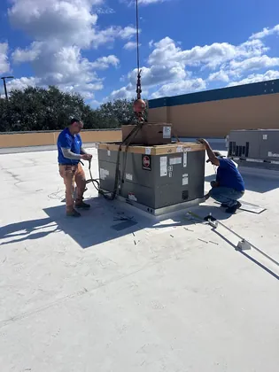 Two Direct Cooling technicians guiding a Rheem commercial rooftop unit onto its curb