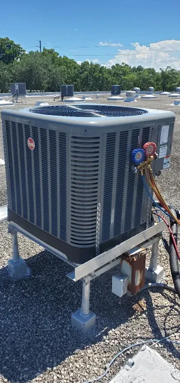 A Rheem condenser on a raised rooftop stand with a refrigerant gauge manifold connected for readings. Refrigerant gauges connected to a Rheem condenser on a raised rooftop stand