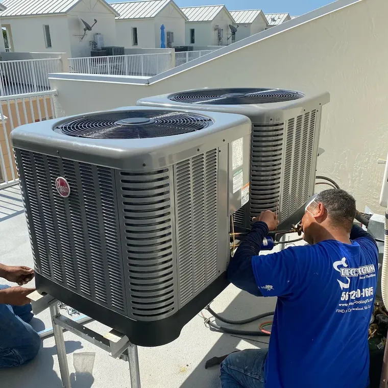 Direct Cooling technician connecting refrigerant lines on two new Rheem condensers on a raised stand