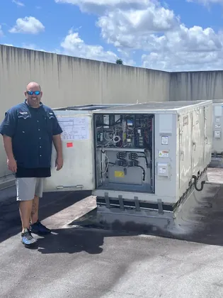 Direct Cooling technician beside a rooftop unit with its control panel open